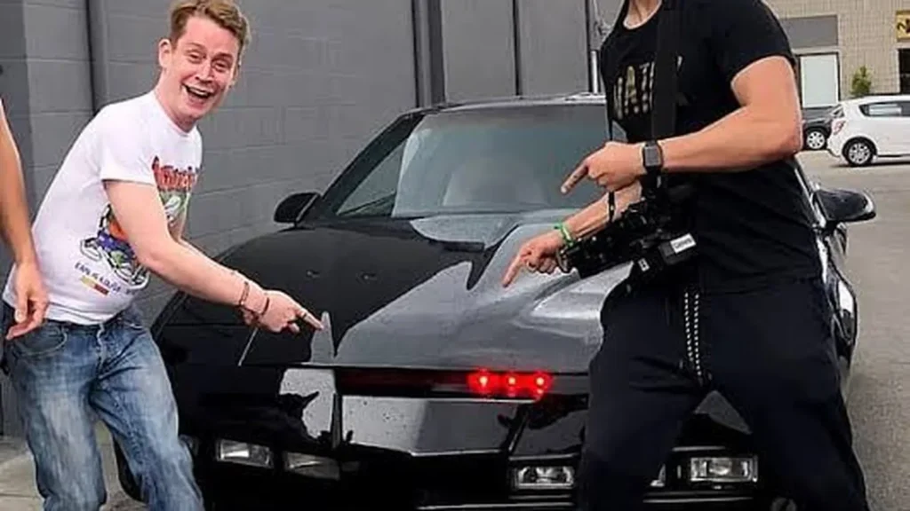 Macaulay Culkin posing beside a classic black car