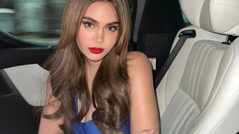 Young woman with long brown hair posing in car wearing blue dress with red lipstick