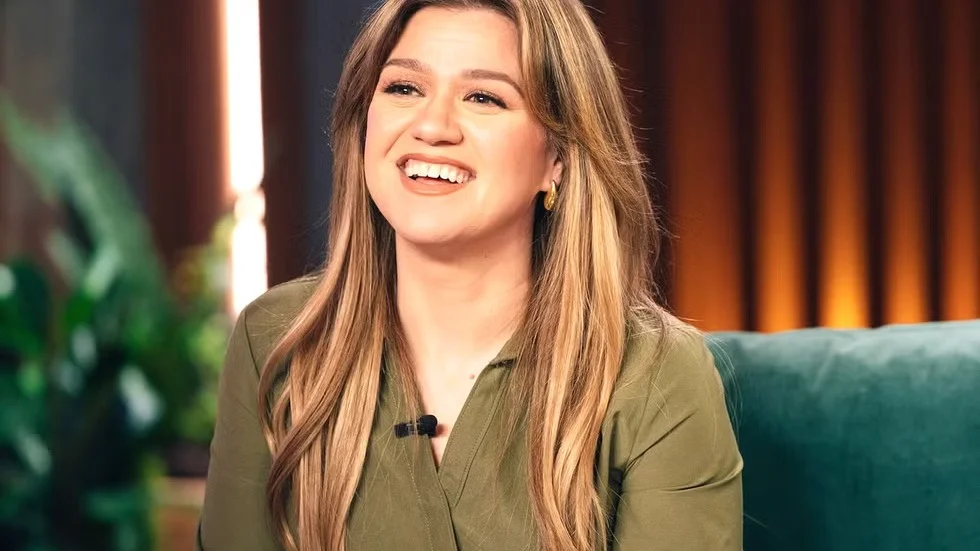 Kelly Clarkson laughing during interview in olive green outfit